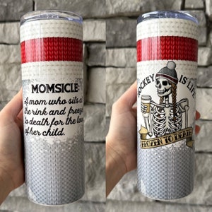 K&ouml;nnte beinhalten: Zwei Edelstahlbecher mit einem wei&szlig;en und roten Strickmuster. Der Becher links tr&auml;gt den Text "MOMSICLE: A mom who sits at the rink and freezes to death for the love of her child." Der Becher rechts zeigt ein Skelett, das einen wei&szlig;en Hut tr&auml;gt und eine Kaffeetasse h&auml;lt. Der Text auf dem Becher lautet "HOCKEY IS LIFE FROZEN TO DEATH."