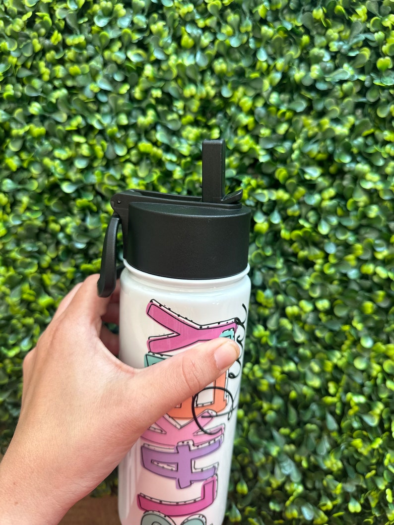May include: White reusable water bottle with a black lid and a straw. The bottle has a colorful design with the word "Kelly" written in a playful font.