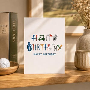 Könnte beinhalten: Eine weiße Grußkarte mit dem blauen Schriftzug HAPPY BIRTHDAY, wobei das Wort BIRTHDAY kreativ aus farbigen Illustrationen von Golfausrüstung wie Tees, einem Golfcart, Schlägern, einer Fahne, einem Handschuh und einem Golfball besteht.