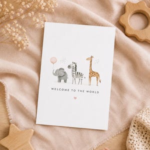 May include: A white rectangular greeting card featuring a watercolor illustration of a gray elephant holding a pink balloon, a black and white zebra, and a brown giraffe. The text WELCOME TO THE WORLD is printed in black below the animals.