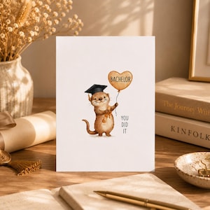 Könnte beinhalten: Eine weiße Grußkarte mit einer Illustration eines braunen Otters, der eine schwarze Doktorhut-Mütze trägt und ein beiges Diplom hält. Der Otter hält einen herzförmigen Ballon mit dem Text BACHELOR und dem Schriftzug YOU DID IT.