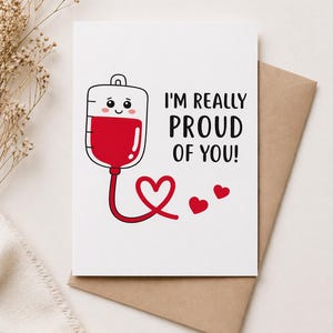 Könnte beinhalten: Weiße Grußkarte mit einer Cartoon-Blutbeutel-Illustration und dem Text "I'M REALLY PROUD OF YOU!". Die Karte enthält ein rotes Herzdesign und liegt auf einem braunen Umschlag.