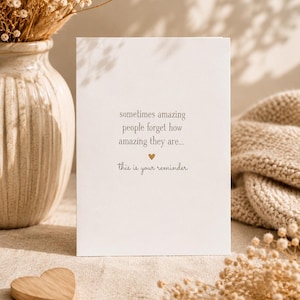 Op de afbeelding: Een witte rechthoekige wenskaart met gecentreerde donkergrijze tekst die luidt: sometimes amazing people forget how amazing they are... gevolgd door een klein gouden hartsymbool en de tekst: this is your reminder.