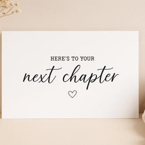 Könnte beinhalten: Eine weiße Karte mit dem Text "HERE'S TO YOUR next chapter" in eleganter Schrift und einem kleinen Herz. Die Karte liegt auf einem neutralen Hintergrund, mit einer Vase mit Trockenblumen und einem Leinentuch.
