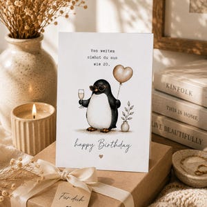 Könnte beinhalten: Eine weiße Geburtstagskarte mit einem schwarz-weißen Pinguin, der herzförmige Sonnenbrillen trägt und ein Sektglas sowie einen herzförmigen Luftballon hält. Die Karte enthält den Text Von weitem siehst du aus wie 20 und happy Birthday.