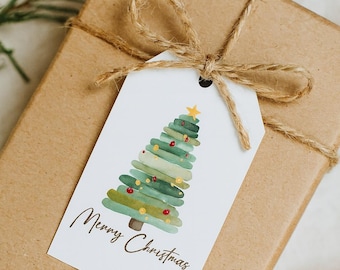 Könnte beinhalten: Ein Weihnachtsgeschenk, verpackt in braunes Papier, mit Bindfaden gebunden und einem weißen Anhänger. Der Anhänger zeigt ein Aquarell-Weihnachtsbaum-Design mit dem Schriftzug "Merry Christmas". Getrocknete Orangenscheiben und Grünzeug sind im Hintergrund.