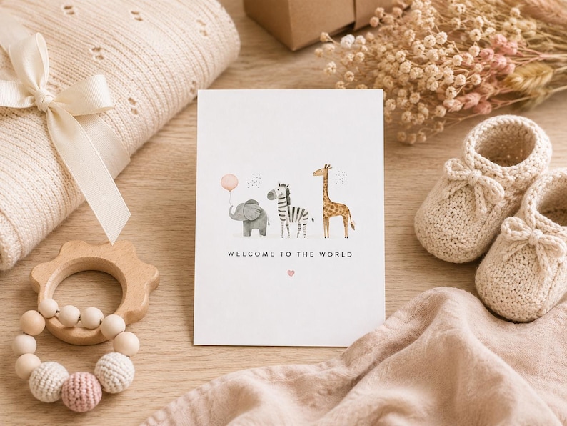 May include: A white greeting card featuring a watercolor illustration of a gray elephant holding a pink balloon, a zebra, and a giraffe. The text "WELCOME TO THE WORLD" is printed in black below the animals, with a small pink heart underneath.