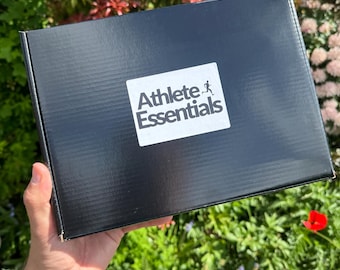 May include: A black box with the text "Athlete Essentials" and a running figure logo. The box is being held in a hand.