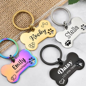May include: Four dog bone-shaped keychains with engraved names and paw prints. The keychains are in gold, silver, rainbow, and black.