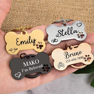 May include: Four personalized dog bone-shaped tags with engraved names and phone numbers. The tags are in gold, silver, black, and rose gold.