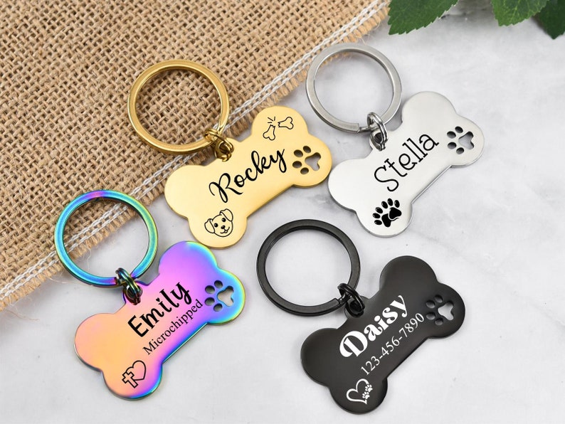 May include: Four dog bone-shaped keychains with engraved names and paw prints. The keychains are in gold, silver, rainbow, and black.