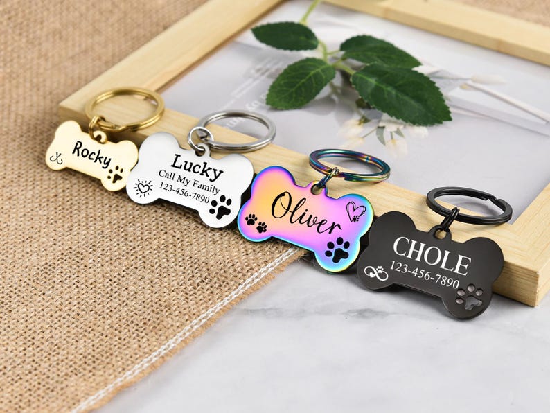 May include: Four dog bone-shaped pet ID tags with engraved names and phone numbers. The tags are in gold, silver, rainbow, and black.