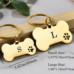 May include: Two gold-tone dog bone-shaped keychains with engraved letters and paw prints. The smaller keychain measures 1.57 inches by 0.78 inches and the larger keychain measures 1.96 inches by 1.18 inches.  Small Size: 1.57*0.78in/4*2cm. Large Size: 1.96*1.18in/5*3cm.