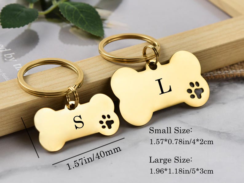 May include: Two gold-tone dog bone-shaped keychains with engraved letters and paw prints. The smaller keychain measures 1.57 inches by 0.78 inches and the larger keychain measures 1.96 inches by 1.18 inches.  Small Size: 1.57*0.78in/4*2cm. Large Size: 1.96*1.18in/5*3cm.