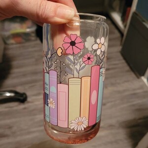 a hand holding a glass with a painting on it