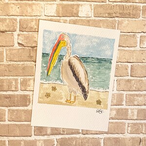 Carte postale peinte à la main Pélican sur la plage, carte postale aquarelle de style Polaroid, papeterie pour amoureux des oiseaux côtiers, correspondance d'été après la traversée