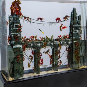May include: A diorama encased in clear acrylic, depicting a bridge scene with miniature figures. The bridge is a dark green color with icicles and figures climbing on it. The figures are red and brown, with some suspended from chains. A missile is in the air.