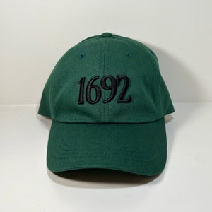 May include: A dark green baseball cap with black embroidered text that reads "1692".