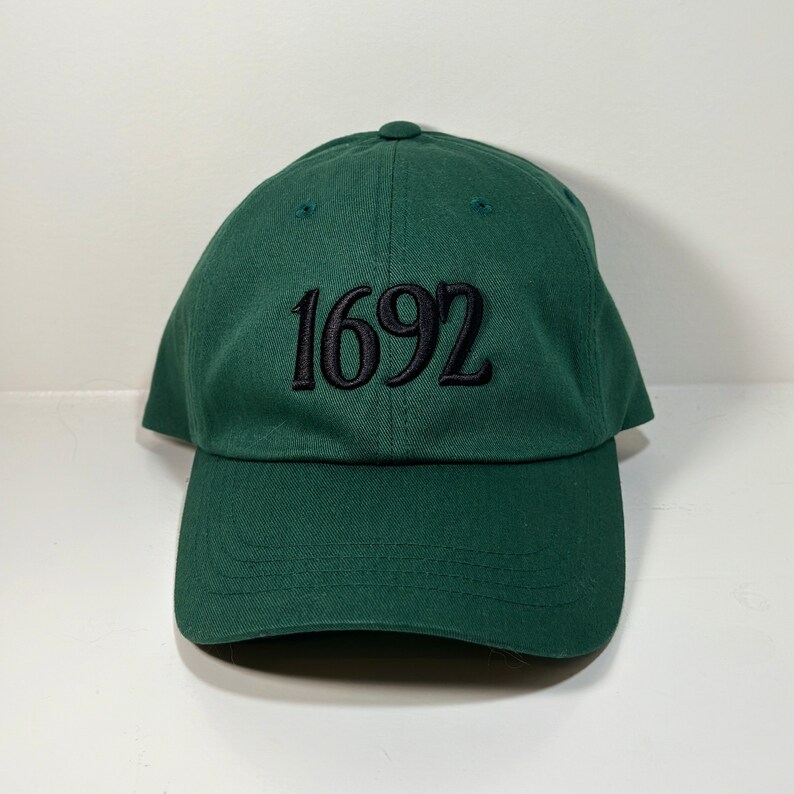 May include: A dark green baseball cap with black embroidered text that reads "1692".