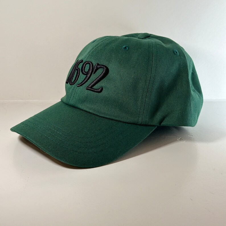 May include: A dark green baseball cap with black embroidered text that reads "1692".