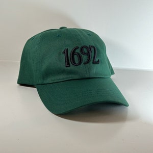 May include: A dark green baseball cap with black embroidered text that reads "1692".
