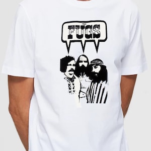 Op de afbeelding: Wit T-shirt met een zwart-witte afbeelding van een band genaamd "The Fugs". De afbeelding toont drie mannen met snorren en baarden.