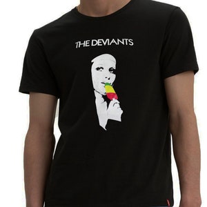 Può includere: Maglietta nera con una grafica bianca di una persona con una maschera che mangia un ghiacciolo verde, giallo e rosso. Il testo "THE DEVIANT" è stampato in bianco sopra la grafica.
