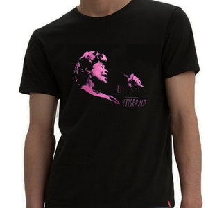 Puede incluir: Camiseta negra con una silueta rosa de Ella Fitzgerald cantando en un micrófono. El texto "Ella Fitzgerald" está impreso debajo de la imagen.