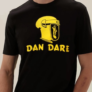 Puede incluir: Camiseta negra con un gráfico amarillo de una persona con casco y el texto "DAN DARE"