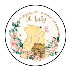 May include: A round sticker with a Winnie the Pooh theme. The image features a yellow bear, a honey pot with the word "HUNNY", a pink butterfly, and the text "Oh Baby". The design is surrounded by flowers and bees.