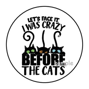 May include: A white circle with black text that reads "Let's face it, I was crazy before the cats." There are three black cats with colorful eyes peeking out from behind the text.