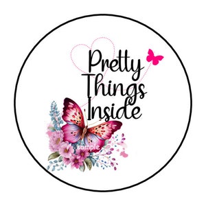May include: A round white sticker with a black border featuring the text "Pretty Things Inside" in black script. A pink butterfly and floral arrangement are below the text. A small pink butterfly is in the upper right.