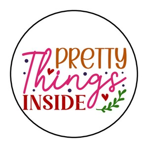 May include: A round sticker with the text "Pretty things inside" in a colorful font. The text is in pink, orange, and red. There are small hearts and dots around the text.
