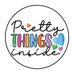 May include: A round sticker with a black outline and the text "Pretty things inside" in black script. The word "things" is in rainbow colors with a small heart in each color.