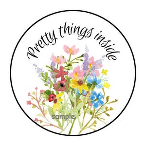 May include: Round sticker with a watercolor illustration of a bouquet of flowers in shades of pink, yellow, blue, and red. The text "Pretty things inside" is written in a black cursive font around the flowers.