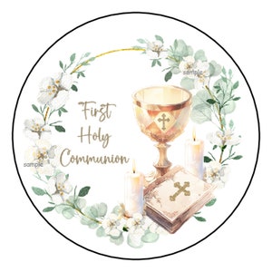 May include: Circular sticker design with a First Holy Communion theme. The design features a golden chalice, a bible, and two lit candles, surrounded by a floral wreath with white flowers and green leaves. The words "First Holy Communion" are written in gold.
