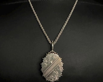 Puede incluir: Un collar de cadena de plata con un colgante de medallón ovalado. El medallón está grabado con un diseño floral.