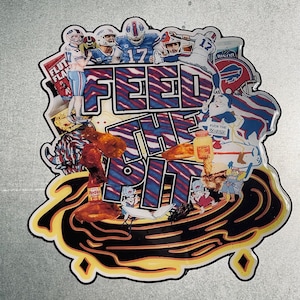 May include: A colorful magnet with the text "FEED THE PIT" in blue and red, surrounded by images of football players, chicken wings, and the Buffalo Bills logo. The magnet has a black and yellow border.