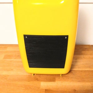 May include: A yellow plastic case with a black, ribbed panel on the front. The case has a handle on the top.