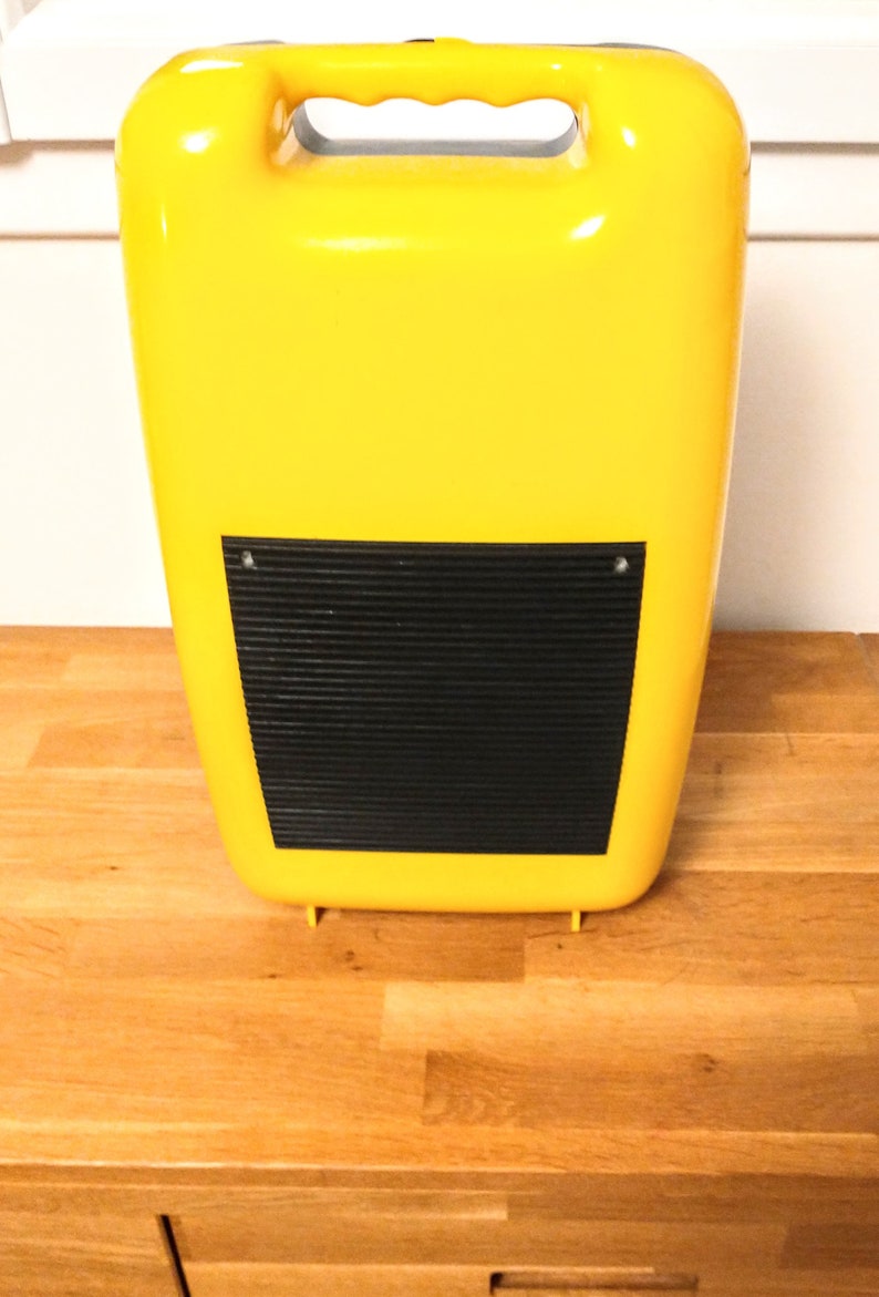 May include: A yellow plastic case with a black, ribbed panel on the front. The case has a handle on the top.