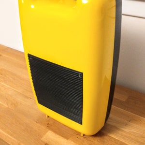 May include: A yellow plastic case with a black handle and a black grill on the front. The case has a rounded shape and a smooth surface.