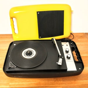 May include: A vintage yellow portable record player with a black turntable and a silver control panel. The record player has a built-in speaker and a carrying handle.