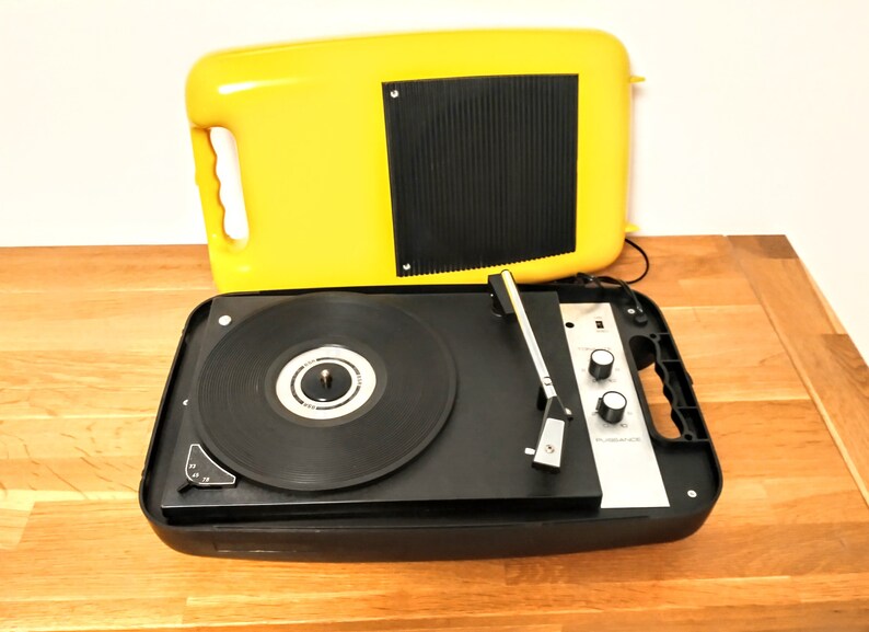 May include: A vintage yellow portable record player with a black turntable and a silver control panel. The record player has a built-in speaker and a carrying handle.