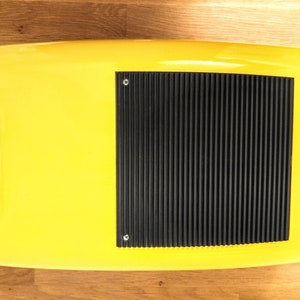 May include: A yellow plastic case with a black rubberised panel on the top. The panel has a series of raised lines and two small screws.