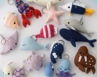 May include: A collection of crocheted sea creature keychains, including a lobster, seal, starfish, fish, shark, whale, seahorse, turtle, octopus, and walrus. Each keychain is a different color and has a metal ring for attaching keys.