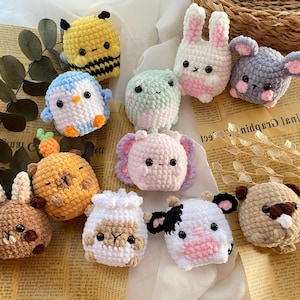 Puede incluir: Una colección de juguetes de animales hechos a mano con ganchillo, que incluyen una abeja amarilla, un pingüino azul y blanco, un oso marrón, un elefante rosa, un conejo blanco, un ratón gris, una rana verde, una oveja blanca y una vaca en blanco y negro.