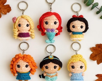 Puede incluir: Colección de llaveros de ganchillo hechos a mano con varios personajes de princesas. Cada llavero muestra un diseño de princesa único con detalles de ganchillo, incluyendo cabello, atuendos y rasgos faciales. Los llaveros están unidos a llaveros de color plateado.