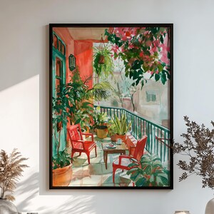 May include: A framed wall art print depicting a sunlit balcony scene with two red chairs, a small table, and various potted plants. The painting features a teal door, lush green foliage, and vibrant pink flowers hanging from above, all rendered in a painterly style.