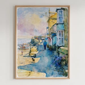 May include: A framed watercolor painting depicting a coastal harbor scene with a stone path, yellow and blue buildings, a person walking, a small dog, and a boat docked in the water. The sky is painted in soft washes of purple, yellow, and blue tones.