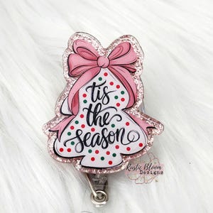 May include: A pink glitter Christmas tree with a pink bow and the text "Tis the Season" in black script. The tree is decorated with red and green polka dots.